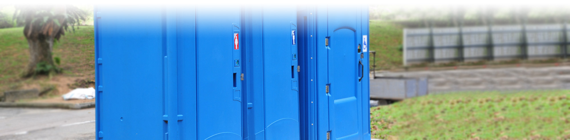 Three blue porta potties included a handicap porta potty in a park